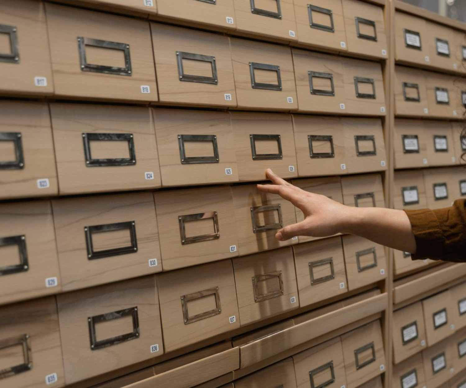 Hand greift in Bibliothekskatalog-Schubladen – Wissensdatenbank oder E-Learning